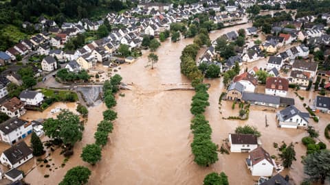 A tree-lined village street flooded with water.